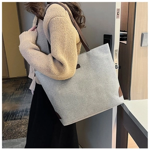 Detail of grey canvas tote bag with brown leather straps shown in a minimalist setting