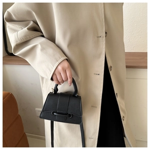 Detail einer schwarzen Minitrapez-Handtasche mit Lychee-Narbenleder und Griff