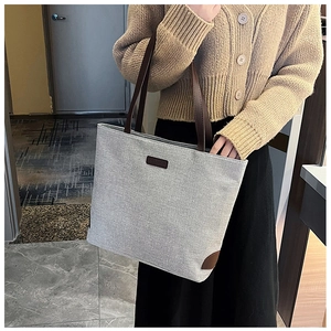 Detail of grey linen tote bag featuring brown leather handles and fashion logo patch