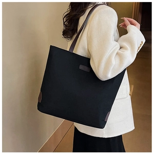 Close-up of black canvas tote bag showing brown leather corner patches and fashion label