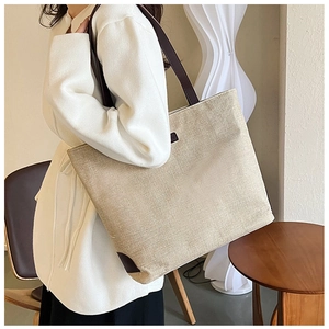 Detail of a large woven tote bag with brown leather handles worn by a model in a minimalist room