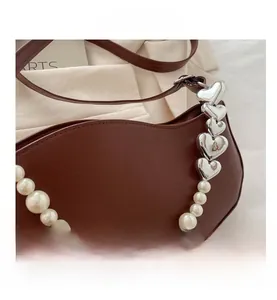 Detail of dark brown leather handbag with pearl chain and silver heart buckle accents