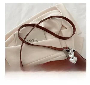 Detail of a brown leather bag with silver heart metal and white pearl chain strap