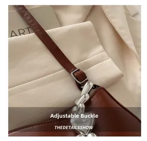 Detail of dark brown leather handbag featuring silver heart chain and adjustable strap