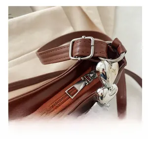 Detail of silver smooth zipper and heart-shaped chain on caramel leather shoulder bag