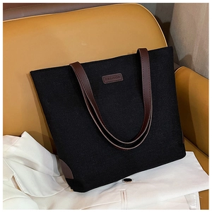 Detail of black linen tote bag with brown leather handles on a stylish yellow sofa