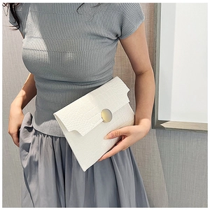 Detail of white crocodile pattern envelope clutch with a gold round metal buckle