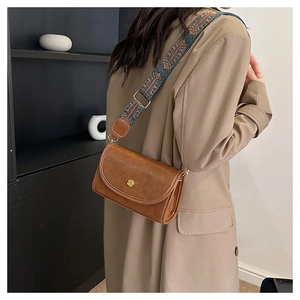 Close-up of retro brown crossbody bag featuring geometric patterned wide strap and floral gold clasp