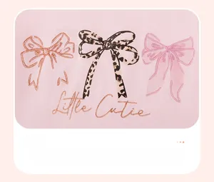 Close-up of pink cotton fabric with cute bow graphics and Little Cutie script embroidery