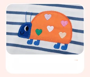 Détail de la broderie coccinelle avec des patchs cœurs colorés sur tissu coton rayé bleu