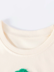 Nahaufnahme des cremefarbenen Strickkleid-Ausschnitts mit feiner grüner Stickerei