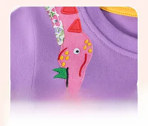 Detail van paarse katoenen jurk met gele halslijn en roze dinosaurusapplicatie