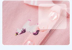 Detail of pink polo dress showing unicorn embroidery and flower-shaped button