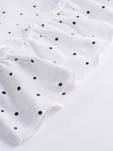 Close-up of white polka dot polo dress fabric featuring delicate ruffle trim details