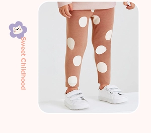 Close-up of brown cotton leggings with white polka dots and white sneakers on child