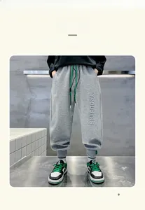 Detail of gray fleece kids joggers featuring green drawstring and TROUSERS embroidery