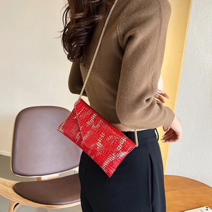 Detalle del bolso sobre rojo con patrón de cocodrilo y elegante cadena dorada