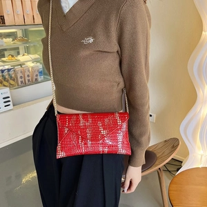 Bolso rojo de moda con patrón de cocodrilo y cadena dorada lucido en una cafetería