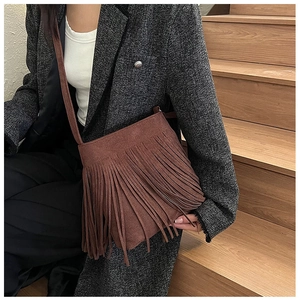 Détail d'un sac bandoulière en daim marron avec de longues franges porté par un mannequin