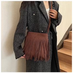 Détail du sac à bandoulière en daim marron avec franges porté sur un manteau d'hiver