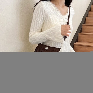 Detailed texture of white wave-patterned knit cardigan with delicate eyelash lace trim