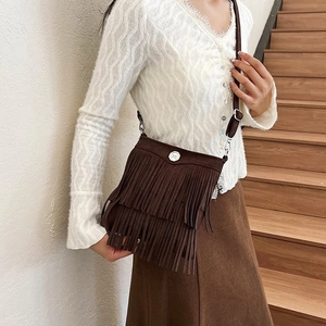 Detail of dark brown suede bucket bag featuring long fringe tassels and silver metal buckle