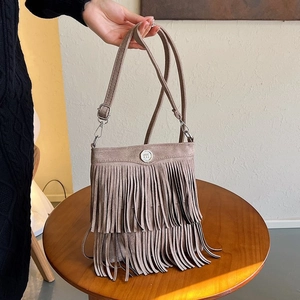 Detail of bohemian brown suede bucket bag featuring long fringe and metallic logo on a table