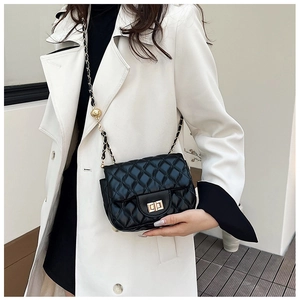 Schwarze Stepptasche mit goldener Kette an einem Modell in einem weißen Mantel präsentiert