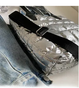 Detail view of silver quilted puffer bag with adjustable black shoulder strap and metal buckle