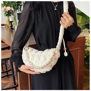 Close-up of a white quilted dumpling bag featuring a pearl chain and ruched strap