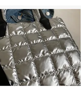Close-up of silver quilted down fabric tote bag with glossy metallic finish and black handles