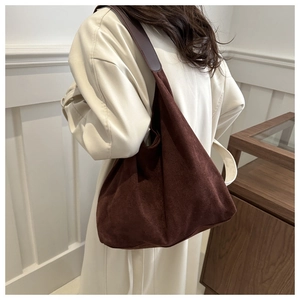 Close-up of brown frosted leather tote bag with wide strap worn with a cream coat