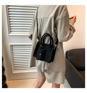 Detalle de bolso negro con textura de cocodrilo y herrajes dorados en una modelo