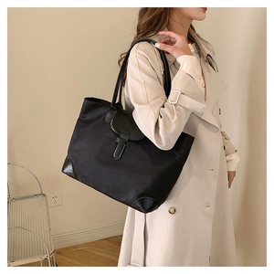 Detail of black nylon tote bag with leather flap and handles on beige trench coat