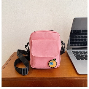 Detail of pink canvas crossbody bag featuring a cute orange patch and adjustable strap