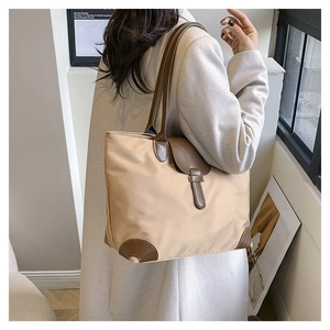 Detail view of a large beige tote bag with brown leather straps and corner reinforcements