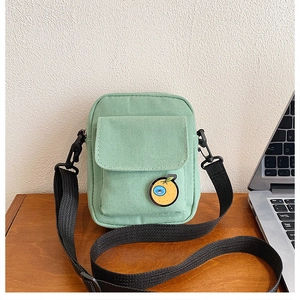 Detail of mint green canvas crossbody bag with cartoon orange badge on wood desk