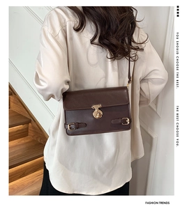 Detail of dark brown vintage crossbody bag with gold buckle on a minimalist background