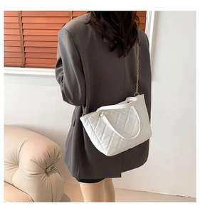 Détail du sac cabas blanc matelassé avec chaîne dorée porté sur un blazer gris chic