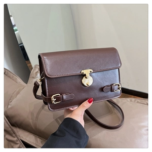 Detail of vintage dark brown crossbody bag with gold T-shaped lock and flap design