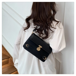 Detail of a vintage black leather crossbody bag featuring gold hardware and a turn-lock clasp