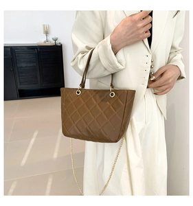 Détail d'un sac cabas marron matelassé avec chaîne dorée sur un blazer blanc chic