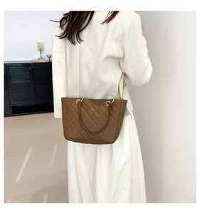 Détail du sac cabas matelassé marron foncé avec chaîne dorée porté par un mannequin