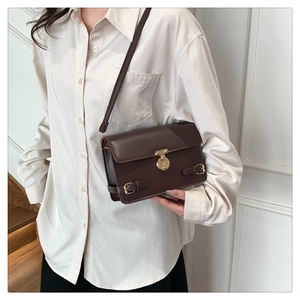 Detail of vintage brown leather handbag with gold metal lock worn over a white shirt