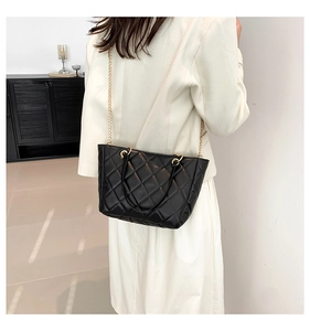 Sac cabas noir matelassé avec chaîne dorée porté à l'épaule par un mannequin