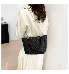 Gros plan d'un sac à bandoulière matelassé noir avec chaîne dorée sur un blazer blanc