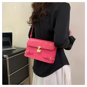 Model wearing a rose pink square shoulder bag with gold clasp and decorative buckle details