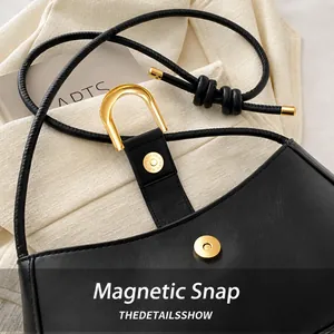 Close-up of black leather handbag featuring a golden magnetic buckle and knotted strap detail