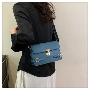 Detail view of a misty blue crossbody bag with a gold circular lock on a model