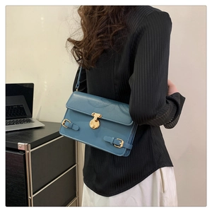 Detail of blue faux leather shoulder bag with gold rotary lock and buckle straps